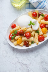 Tortiglioni pasta with roasted cherry tomatoes and burrata cheese, vertical shot on a white stone background, high angle view