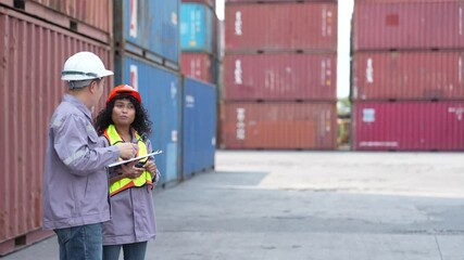 Two engineers in safety gear discuss logistics using a digital tablet at a container yard, representing teamwork in industrial operations. - Powered by Adobe