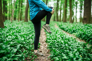 Runner woman stretching legs and quadriceps before jogging and running in forest, warming up exercise routine