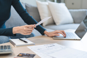 Stressed asian young business woman, employee using laptop computer to calculate expenses, hand holding bills and receipt for to payment on table at home. Financial, finance of banking concept.