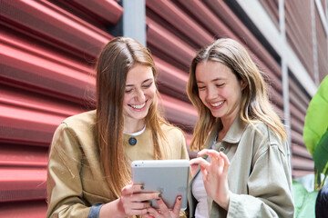 Two young women smiling and using a tablet in urban setting