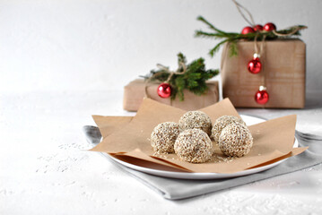  A charming display of oatmeal energy balls coated with sesame seeds sits on brown paper, surrounded by festive decorations. Red ornaments and gift boxes add a cozy holiday touch, perfect for celebrat