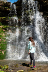 Fototapeta premium Young woman standing in front of a spring waterfall