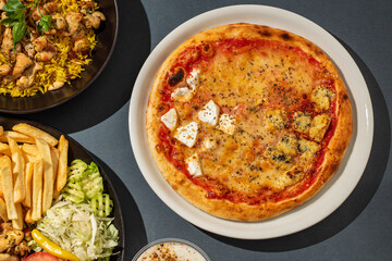 Pizza, chicken sandwich, French fries, rice and other food served on a table, top view