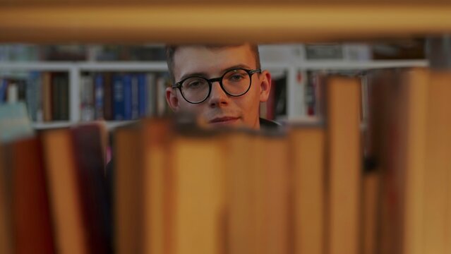 A thoughtful reader sits in a library, surrounded by books and shelves, engaging in reflection. Media