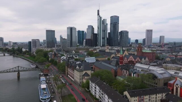 Aerial view of Frankfurt, Germany, showcasing the Main River, Eiserner Steg bridge, boats, modern skyline, historic architecture, and tree lined streets.