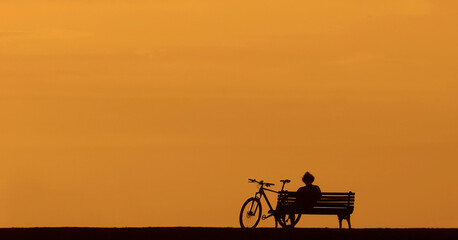 black Silhouette of a man one alone sitting on the bench with his bicycle by hill of Kalemegdan,...