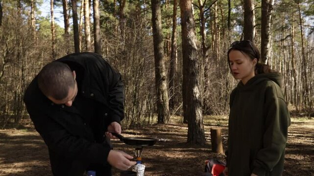 Cooking in nature during a camping trip, as a couple shares tasks at a small forest clearing&mdash;capturing the experience of slow food, companionship, and minimalist outdoor gear