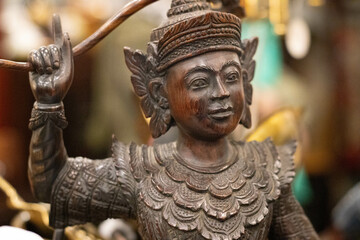 Intricately Carved Wooden Statue of a Traditional Southeast Asian Deity or Mythological Figure with Ornate Headdress, Layered Armor, and Expressive Facial Features, Representing Cultural Heritage, Spi