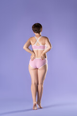 Slim woman in pink underwear on purple background, full length body care concept