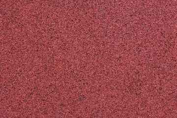 Red sports field rubber coating close up macro view. Playground paving background texture extremely...