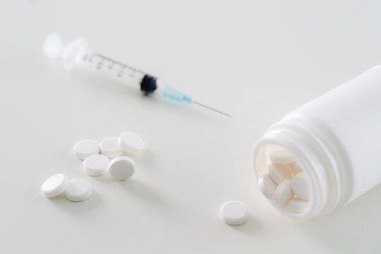 A syringe and a bottle of pills are on a white table. Concept of caution and responsibility