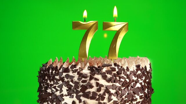 Burning candles number 77 on birthday cake against chroma key background. Seventy-seventh birthday. Birthday celebration