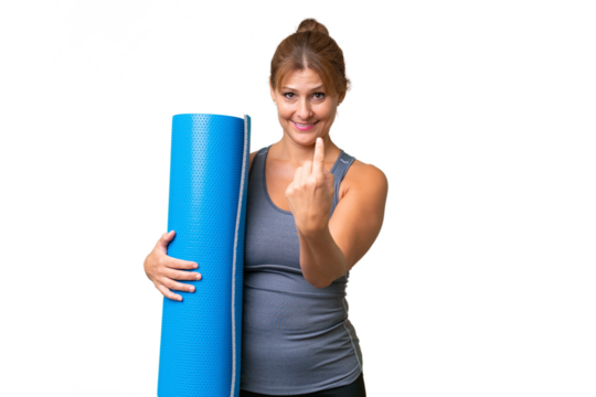 Middle-aged sport woman going to yoga classes while holding a mat over isolated background doing coming gesture