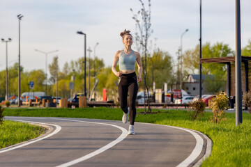 a young woman in sports clothes running along an asphalt path in a park