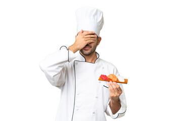 Young caucasian chef holding a sushi over isolated background covering eyes by hands. Do not want to see something