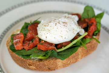 delicious breakfast poached egg on a slice of ciabatta with spinach and pieces of red salted fish