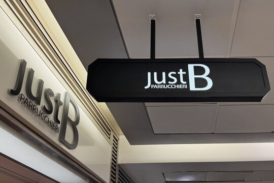 Milan, Italy - April, 07, 2025: Just B Parrucchieri illuminated black and white salon sign indoors. Modern branding of hair salon in Milan, Italy.