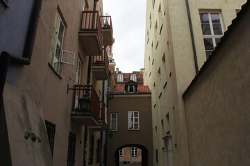 Quiet narrow passageway with red balcony railings, dormer windows, and aged stucco walls in an old...