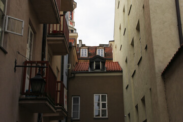 Quiet narrow passageway with red balcony railings, dormer windows, and aged stucco walls in an old...