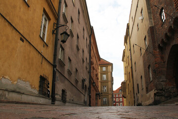 Low-angle view of a narrow cobbled street lined with historic buildings in a European old town, cloudy sky above