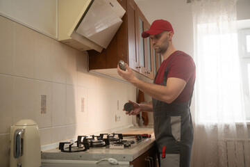 Professional technician wearing a red cap and uniform, methodically repairs a gas stove in a kitchen, using tools and expertise to ensure proper function and safety