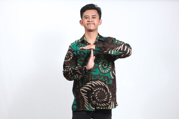 Asian man wearing batik shirt asking for extra time by pointing hand symbol. isolated on white...