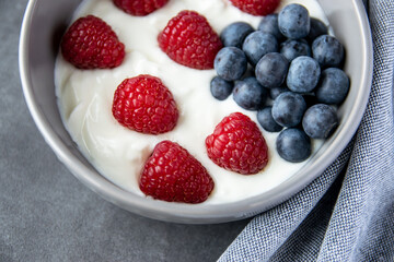 Gray bowl and natural yogurt with berries on the stone background.