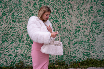 Elegant woman wearing white fur holding handbag and checking smartphone