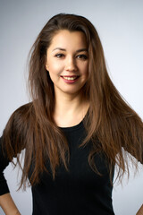 Naklejka premium Portrait of Beautiful Smiling Young Woman. A gorgeous woman with long brown hair against a plain light grey backdrop