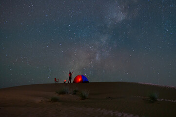 Fototapeta premium A man camping tent in beautiful night stars milky way at emptied desert sand dune 