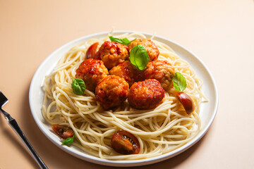 Spaghetti and meatballs with tomato sauce, basil and cherry tomatoes on a plate on a bright background