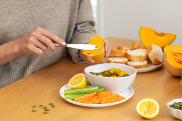 Woman preparing pumpkin spread with fresh vegetables on wooden table. Pumpkin hummus