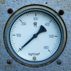 Close-up of a round analog pressure gauge mounted on a textured metal surface.