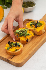 Woman's hand takes delicious bruschetta with pumpkin hummus and microgreens on wooden board