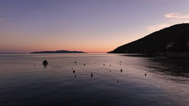 Slow motion minimalistic sunset above the Adriatic Sea. View from the port of Lovran, Croatia. Calm water surface and clear sky with pink, orange and blue colours.