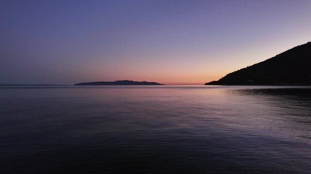Slow motion minimalistic sunset above the Adriatic Sea. View from the port of Lovran, Croatia. Calm water surface and clear sky with pink, orange and blue colours.