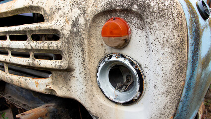 Close-up of the front of a heavily weathered and rusted vehicle, showing a missing headlight and an...