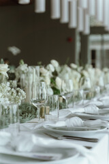 Wedding. Banquet. The chairs and round table for guests, served with cutlery, flowers and crockery and covered with a tablecloth,  green and white theme.