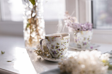 A porcelain teacup with freshly brewed coffee, delicate foam, and rising steam, placed beside a...