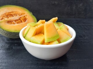 Fresh melon slices in bowl on black wooden table background. Healthy food lifestyle 
