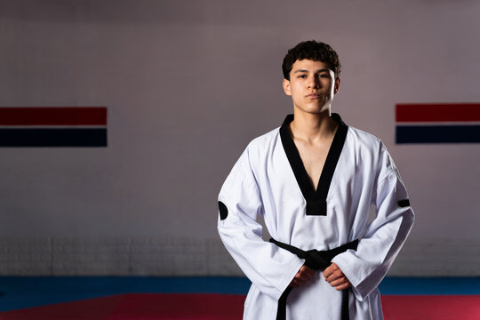 Young taekwondo fighter wearing dobok and black belt posing in gym