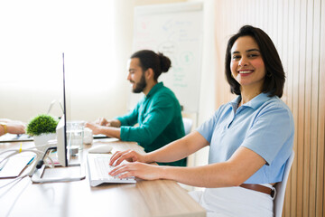 Fototapeta premium Smiling businesswoman typing on keyboard working in modern office with colleagues