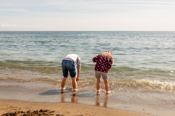 Two girls, fully dressed, playing with sand and waves and dipping their feet into the Mediterranean water, having a fun, joyful time. Children at the beach when it is too cold to swim