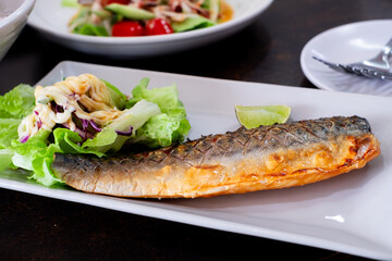 Grilled mackerel served on a white plate with fresh green salad, topped with creamy dressing and a slice of lime. A healthy and delicious seafood dish perfect for food content
