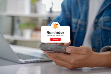 Reminder notification on smartphone while casual man working remotely at home office, representing...