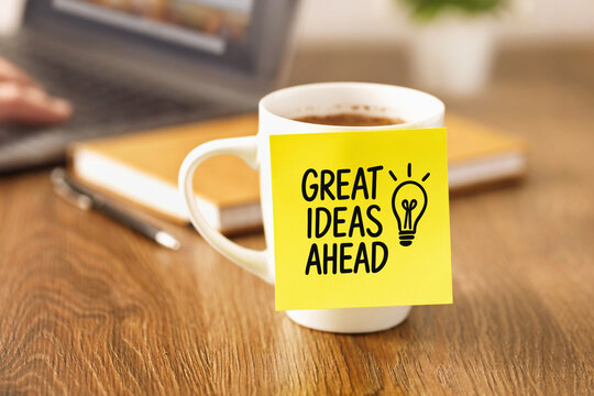 Coffee cup with yellow sticky note showing great ideas ahead message on wooden desk workplace motivation inspiration creativity productivity goal planning startup concept