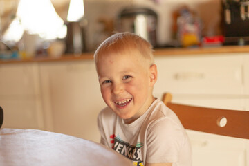 Naklejka premium A delighted young boy happily enjoys a precious moment at the kitchen table, joyfully spreading happiness all around him
