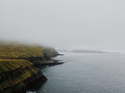 Dramatic Coastal Rock Formations Shrouded in Thick Fog Over Calm Northern Sea - Powered by Adobe