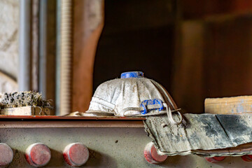 A dusty protective mask and work glove lie on a metal shelf in an abandoned carpentry workshop. Traces of intensive work and dirt indicate long-term use in difficult conditions.
